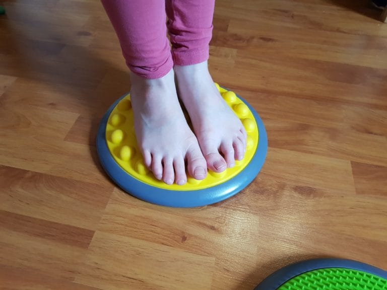 Gros plan sur les pieds d'un enfant explorant une dalle tactile verte sensorielle
