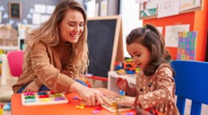 Enseignant et une petite fille jouant avec un jeu de puzzle mathématique assis sur une table à la maternelle